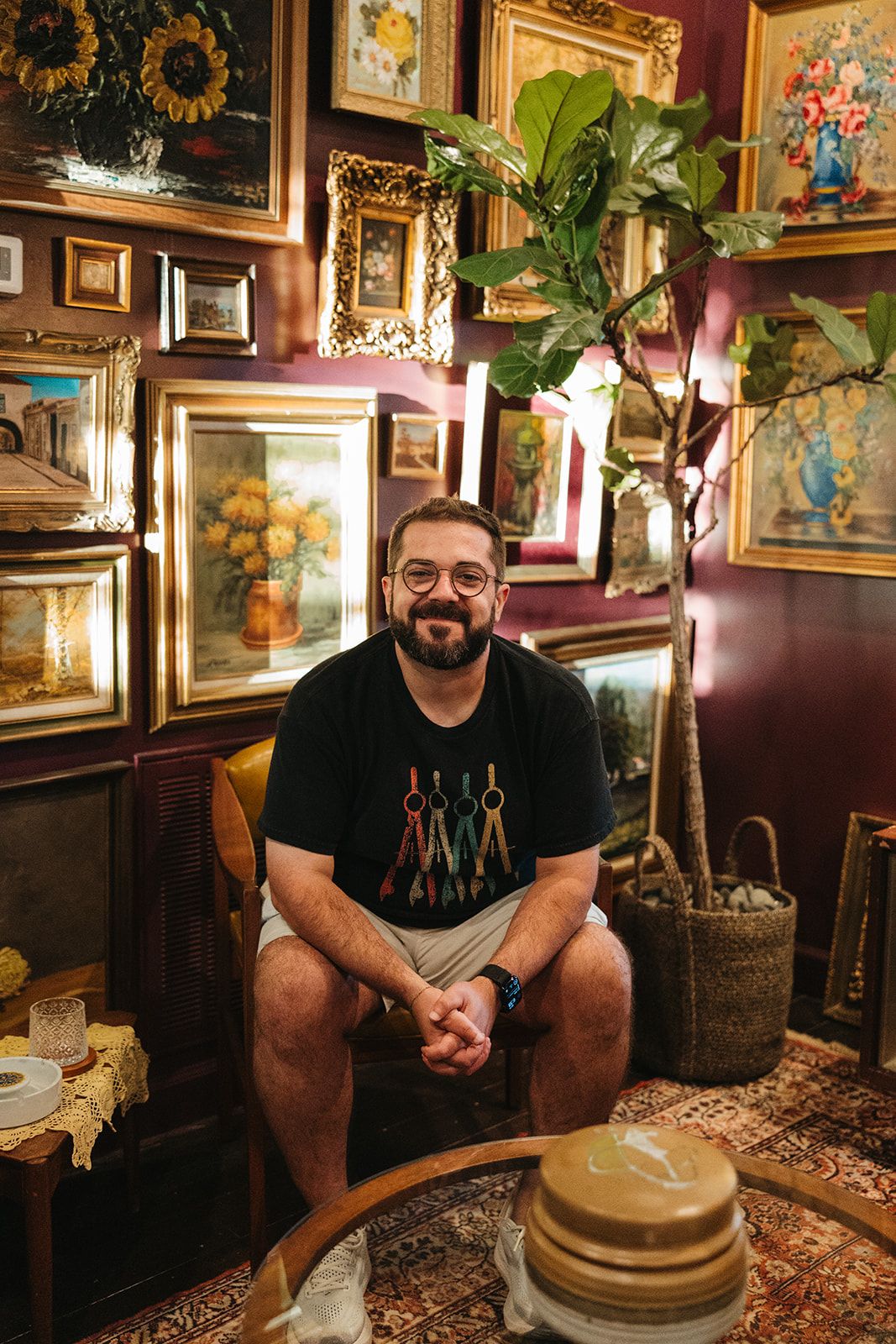 A man seated in the salon posing in front of a wall of framed art
