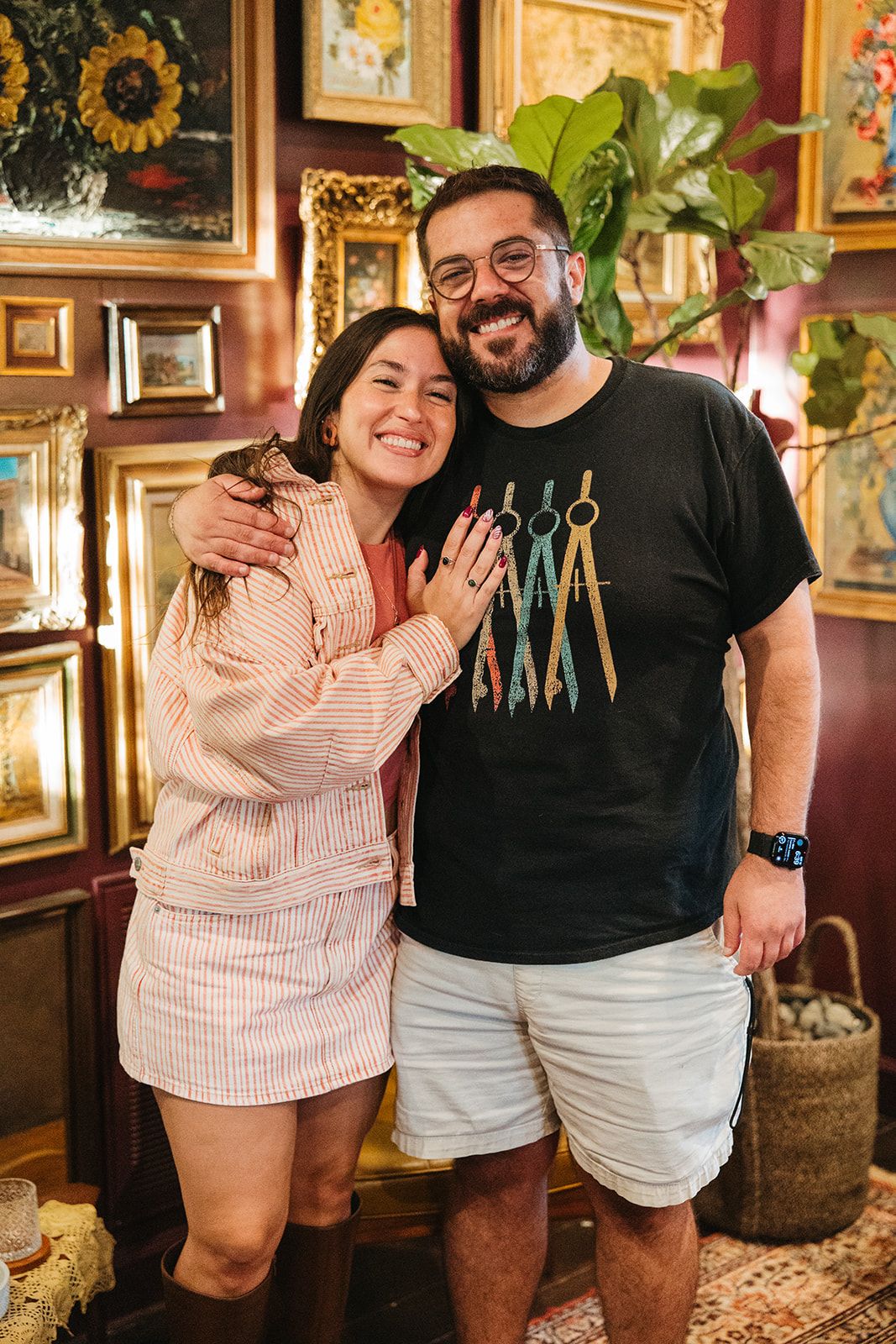 A couple in coordinated outfits posing in front of the gold-frame gallery wall