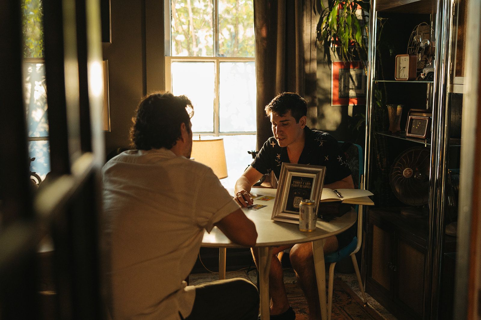 Two people talking at a round table beside a sunny window