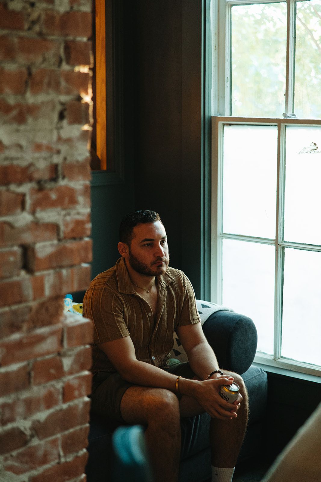 A man seated by a brick wall and a window