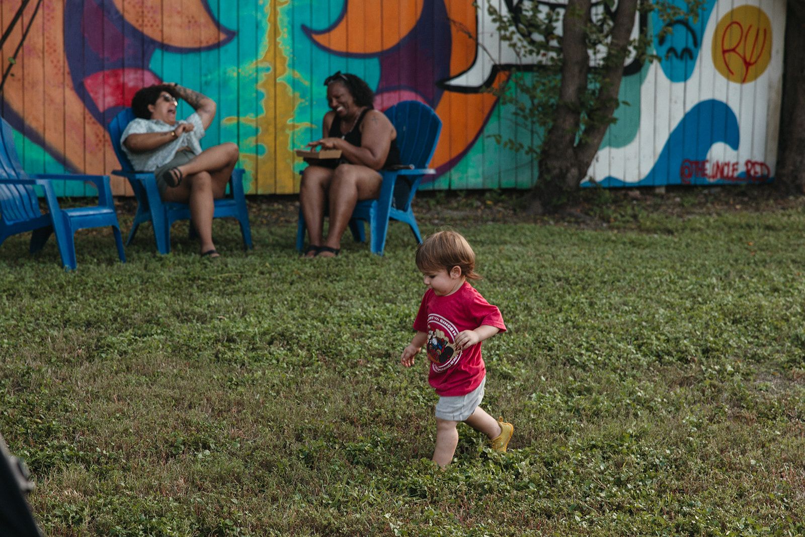 Kids playing on the lawn while family sits on chairs by a mural