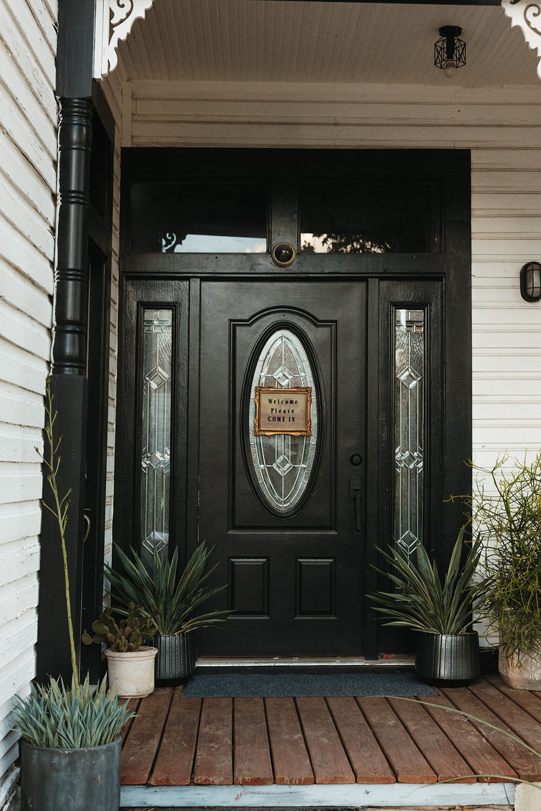 Black front door with an oval glass window and potted plants on the porch