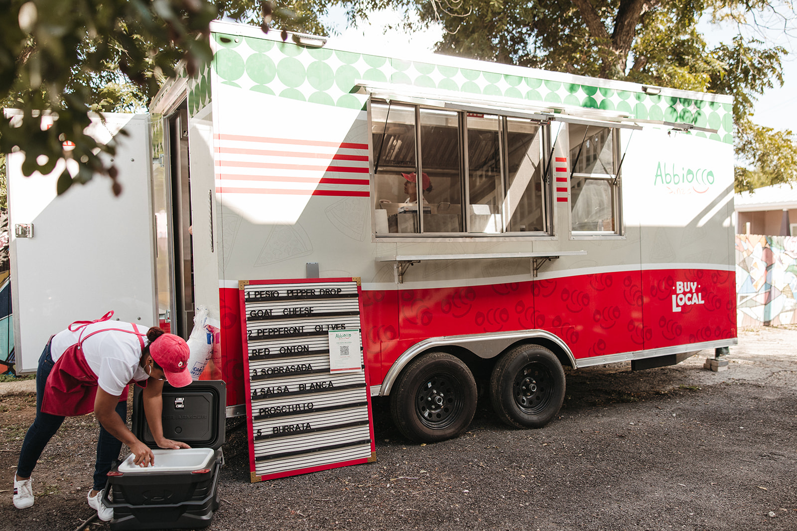 A red and white food trailer in the yard with a vendor setting up