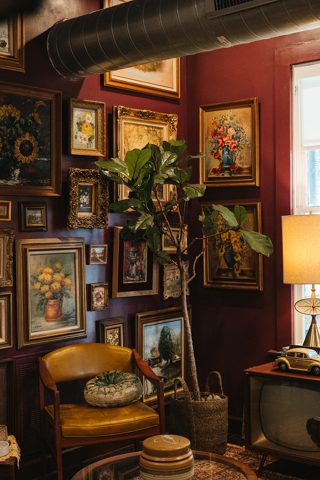 Corner with gold frames on the wall, a mustard chair and a lamp