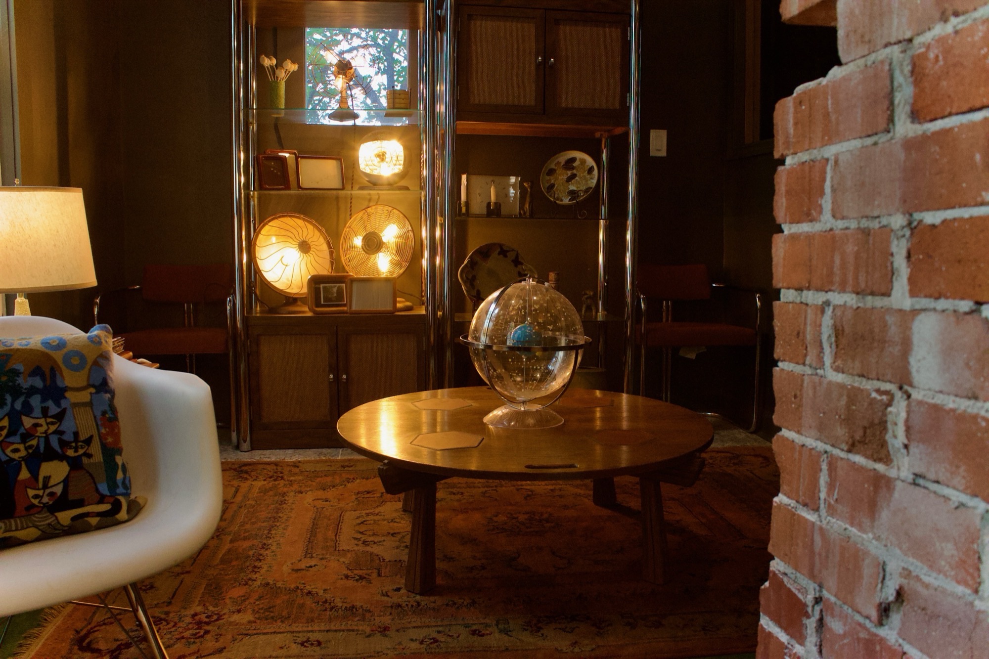 The studio room with a round wood table, a white chair, a globe, a lit cabinet and brick