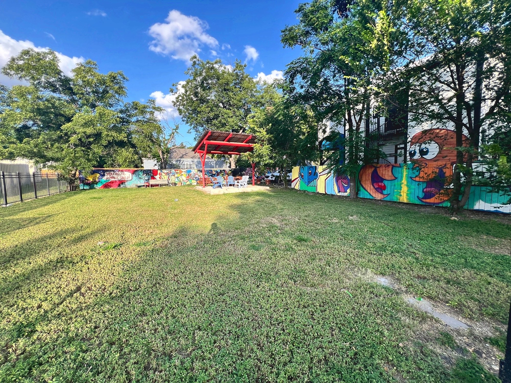 A wide open lawn with mural-painted fences and a red pavilion