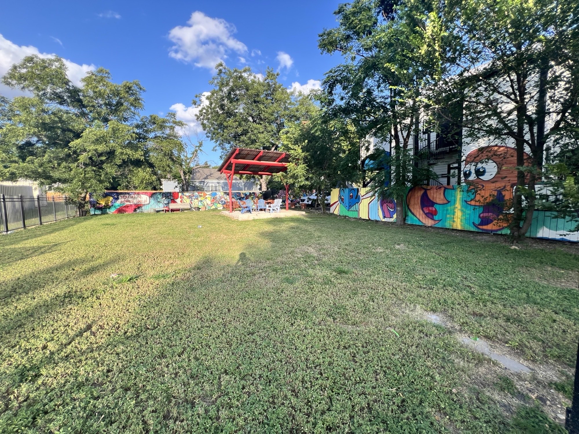 Wide open lawn with mural-painted fences, a red pavilion in the back and trees
